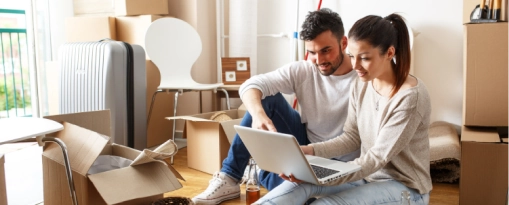 Man and woman sat next to their house-moving boxes using a laptop